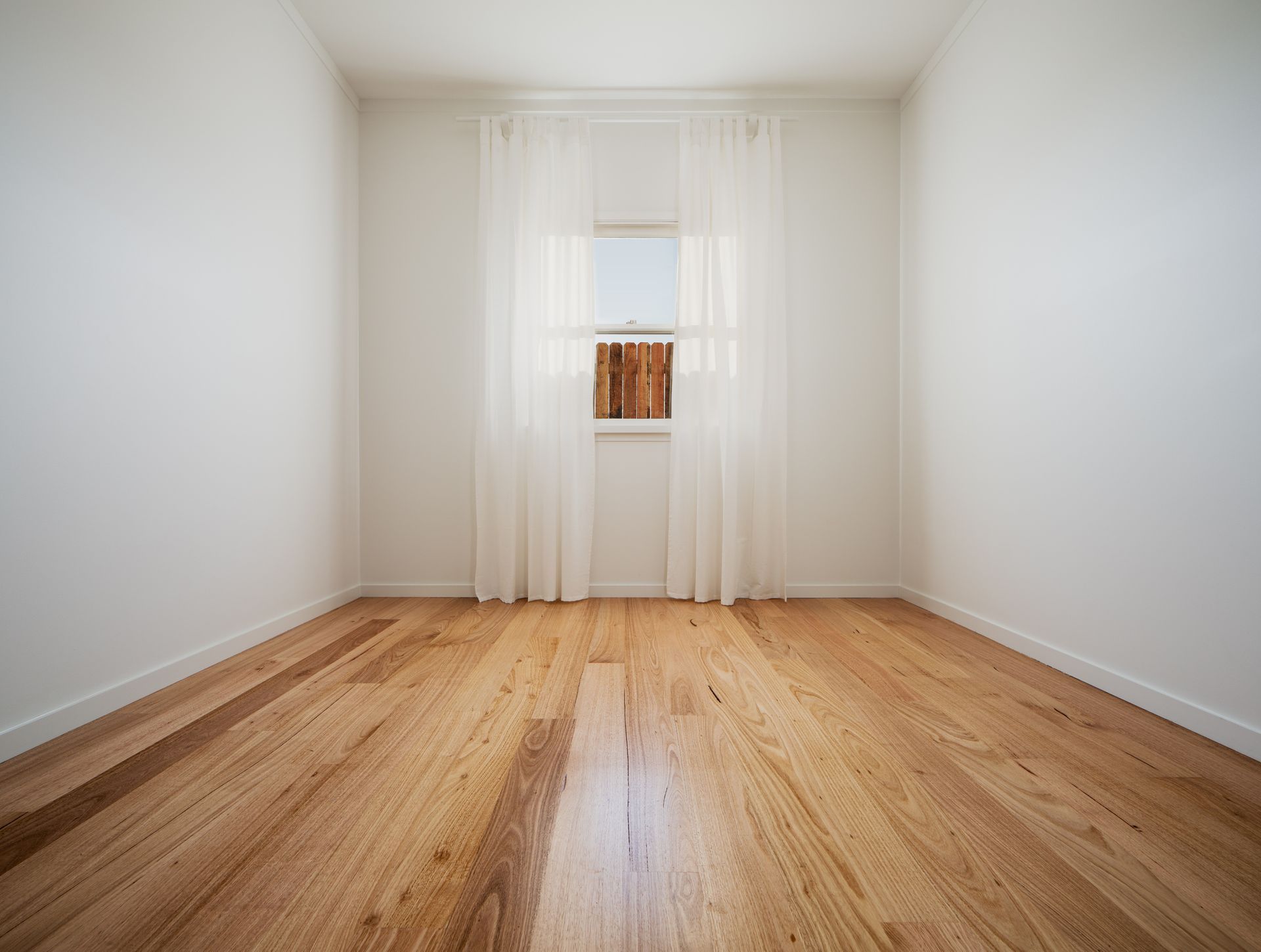 An empty room with hardwood floors and a window.