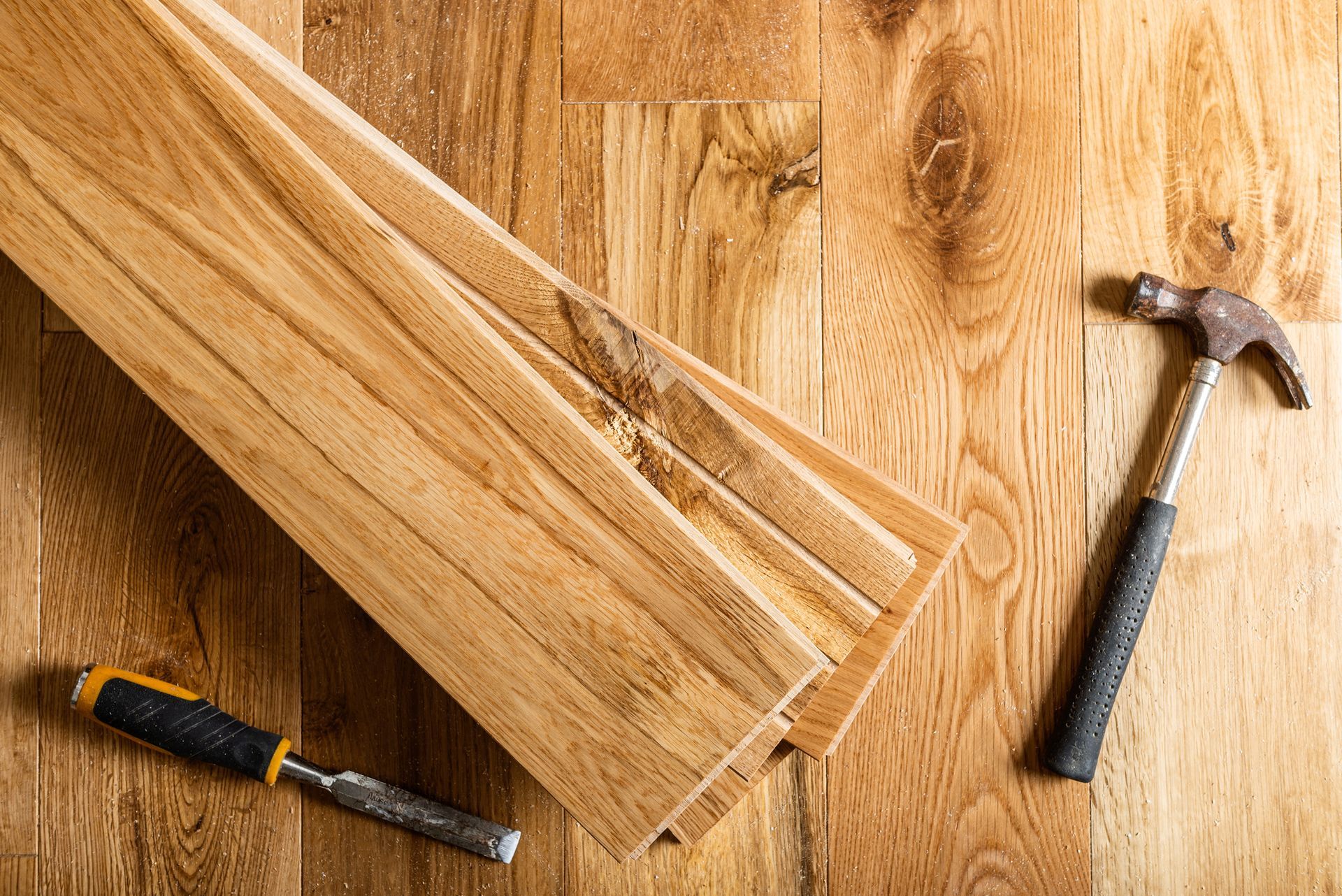 A hammer , chisel , and piece of wood on a wooden floor.