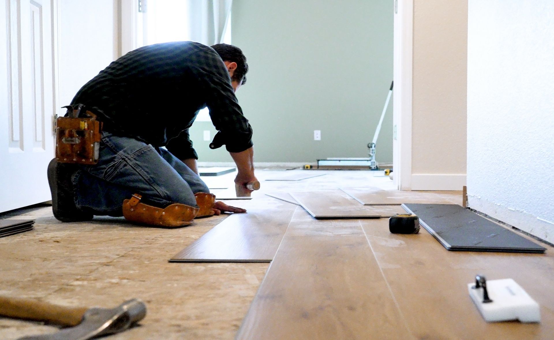 A man is kneeling on the floor while installing hardwood flooring.