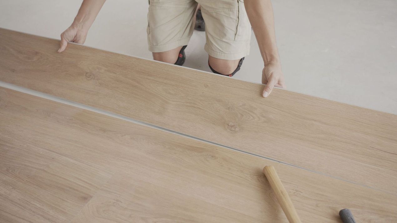 A man is kneeling down to install a wooden floor.