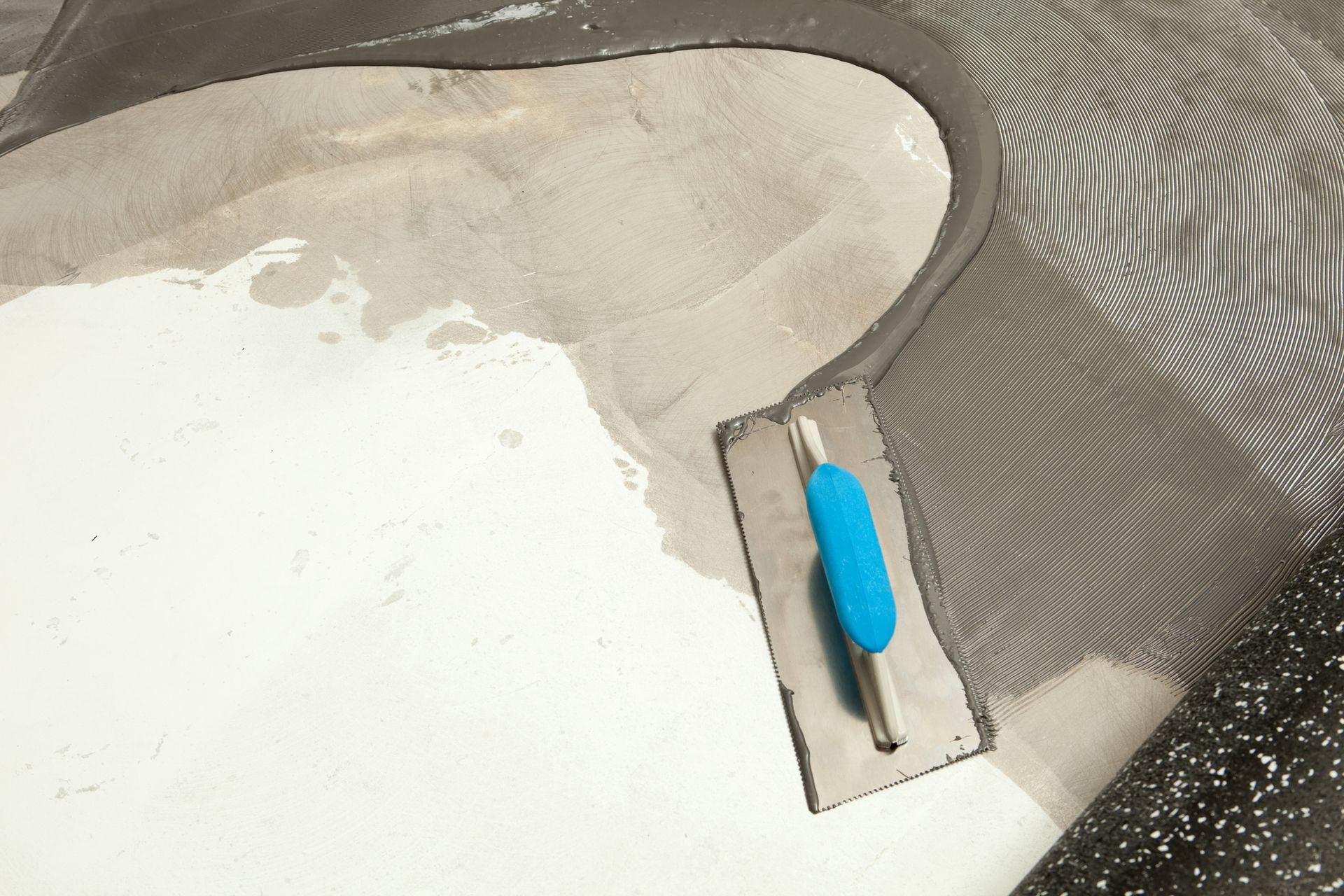 A trowel with a blue handle is laying on a white surface.