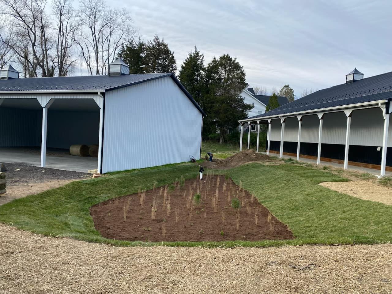 A white barn with a black roof is sitting next to a pond stabilizaion project.