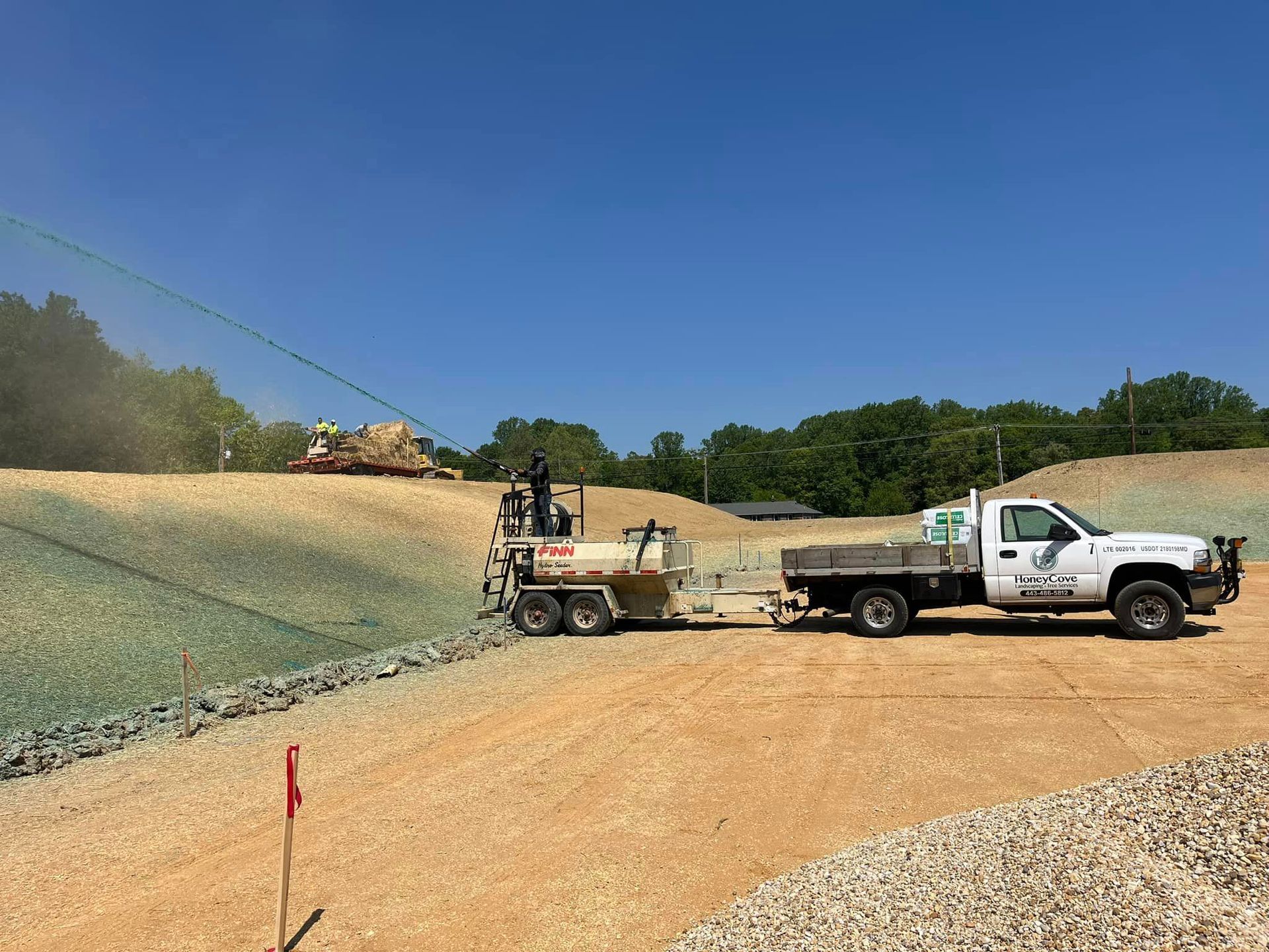 A white truck with a trailer attached to it is parked in a dirt field.