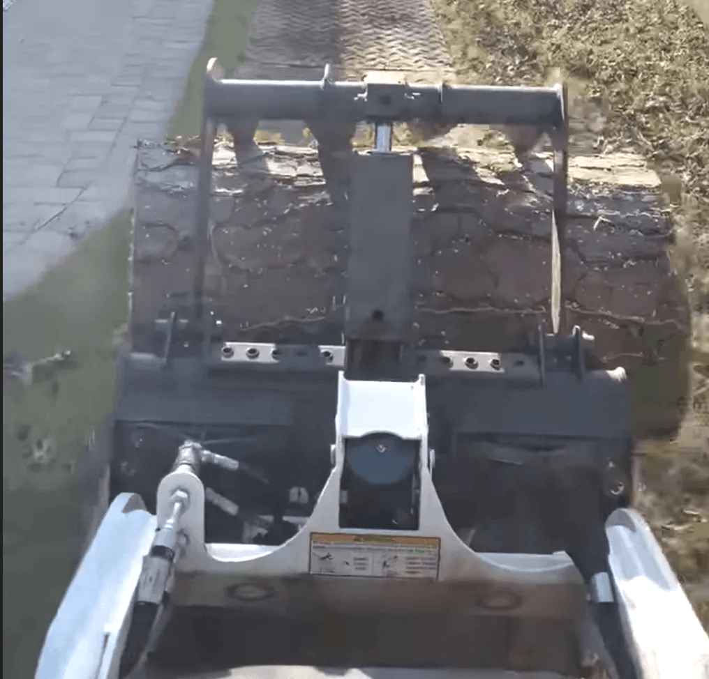 A bulldozer is moving a large log down a sidewalk.