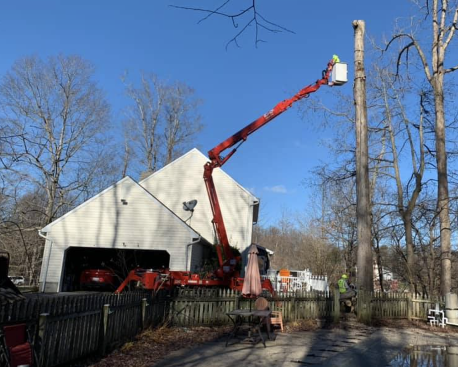 A crane is cutting a tree in front of a house.