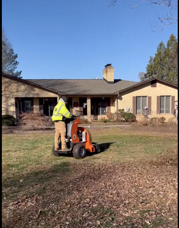 A man is riding a lawn mower in front of a house.