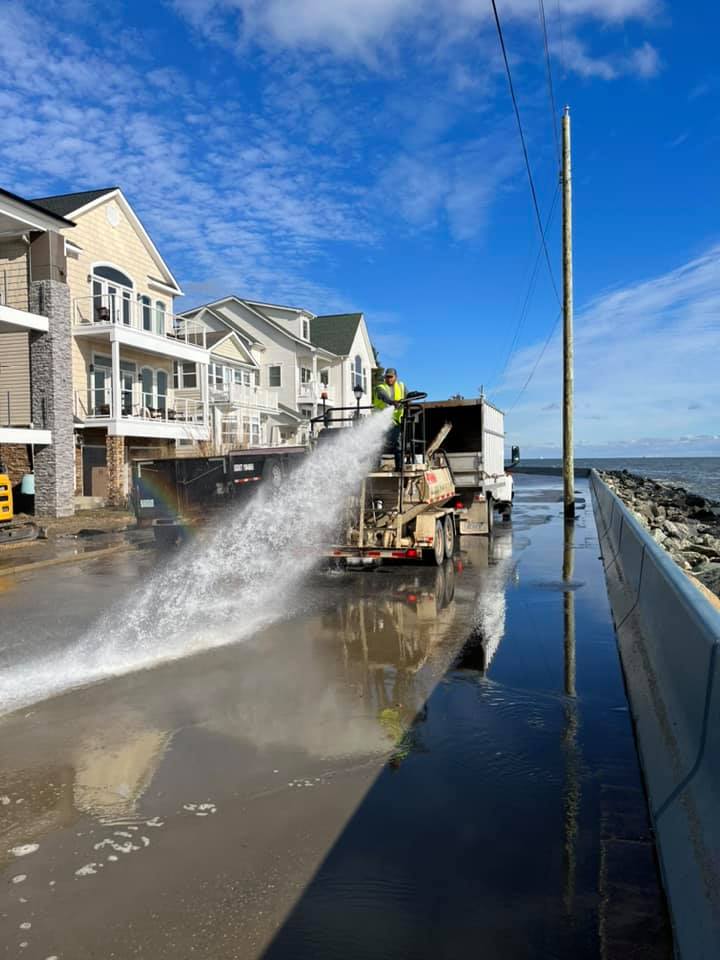 A man is spraying water on a street after storm damage.