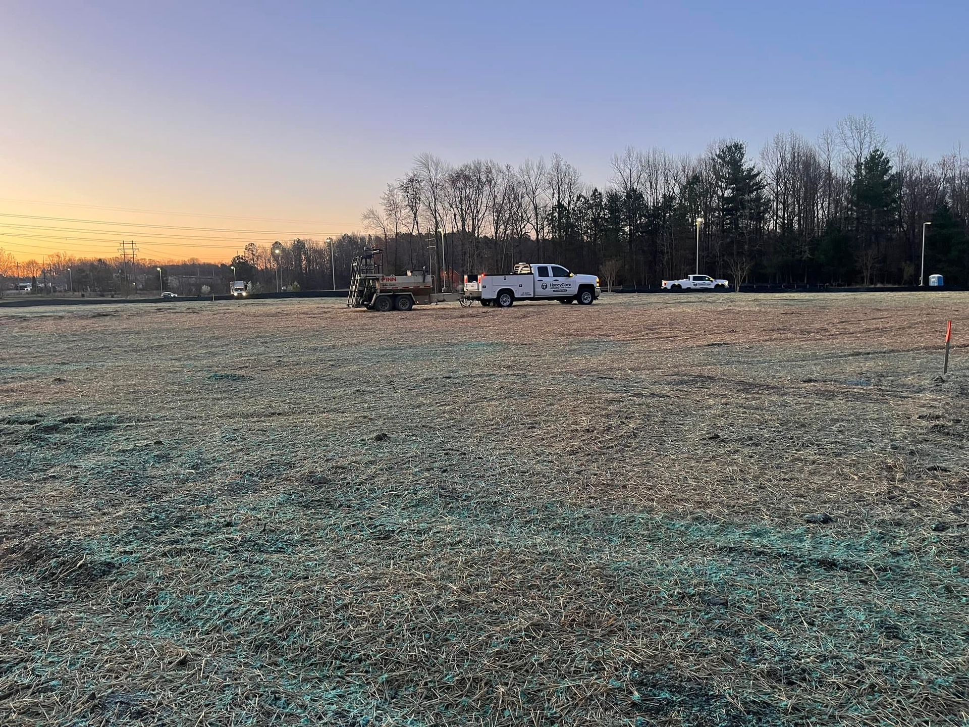 A white truck is parked in the middle of a field working on hydroseeding.
