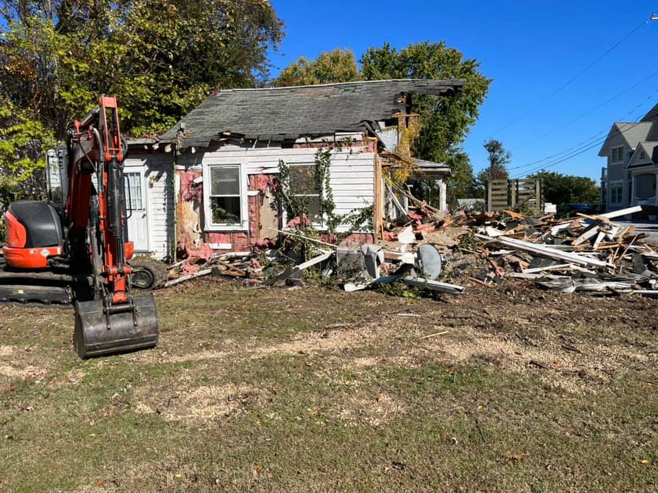 A house is being demolished with an excavator in the foreground.