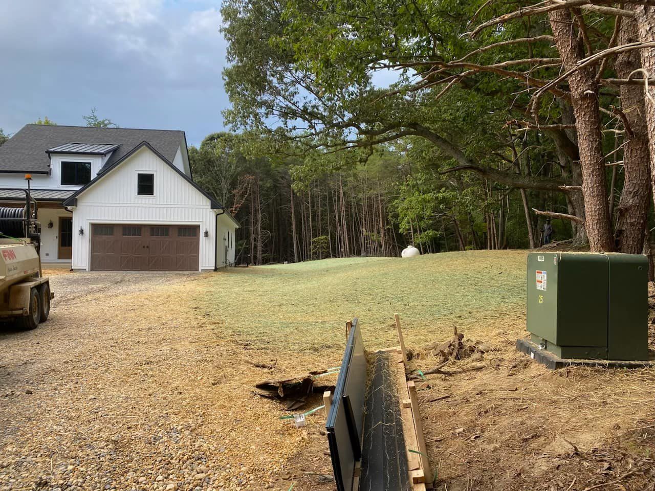A white house with a brown garage door is sitting on by a stabilization area.