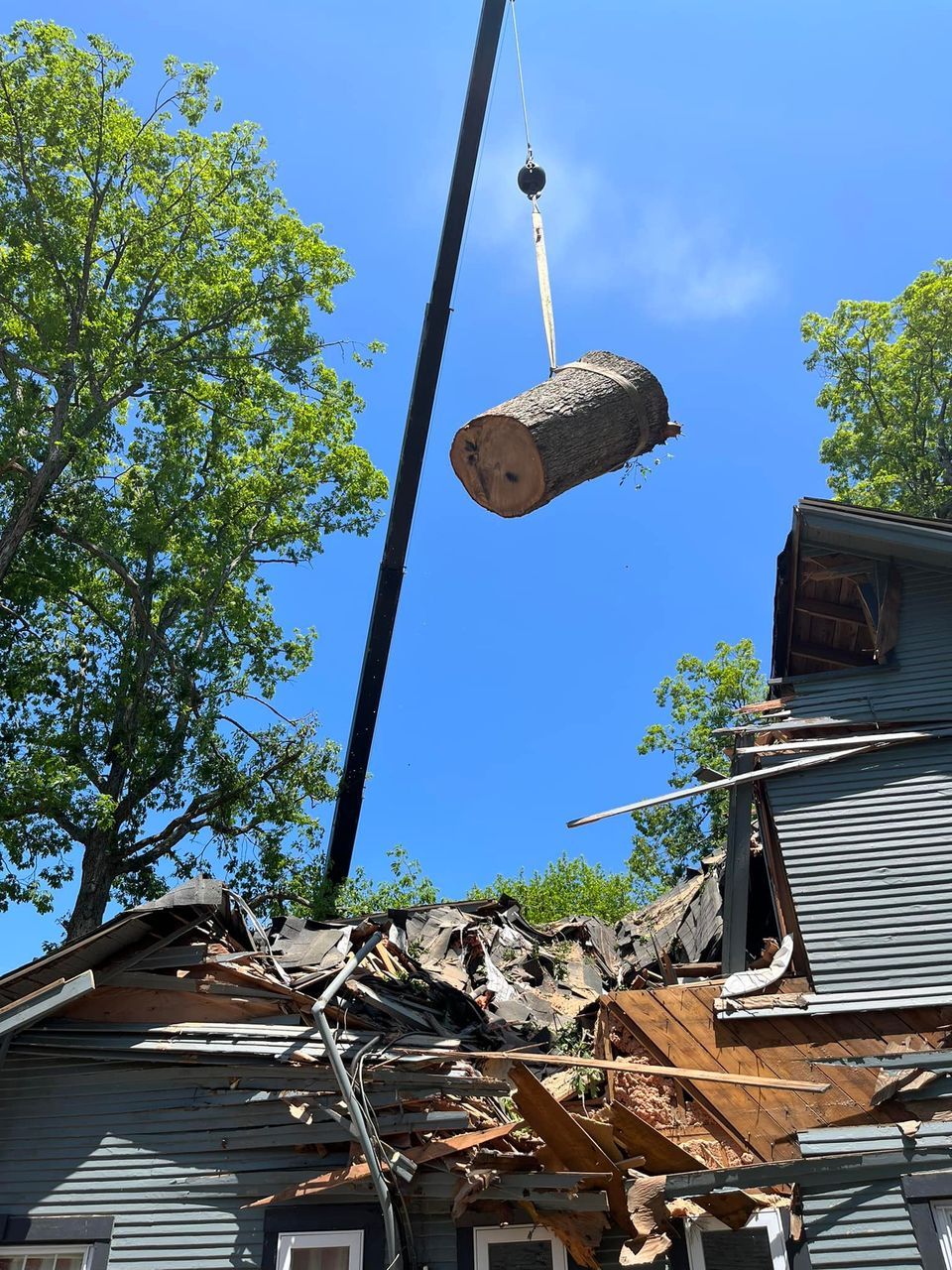 A large log is being lifted by a crane over a house.