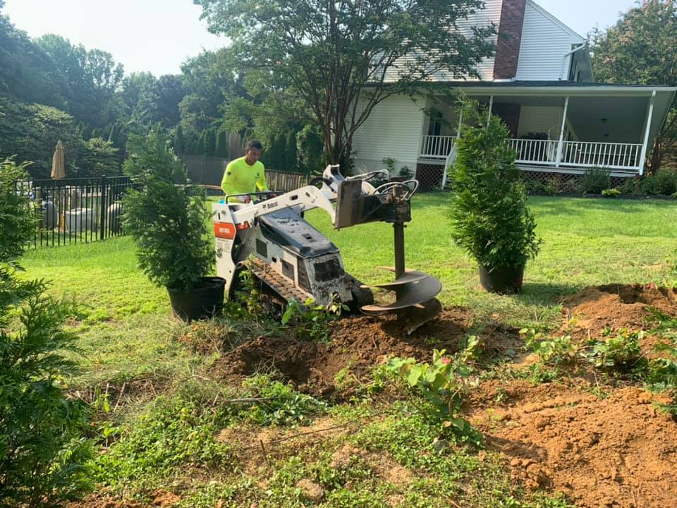 A man is using a machine to dig a hole in the ground to plant trees.