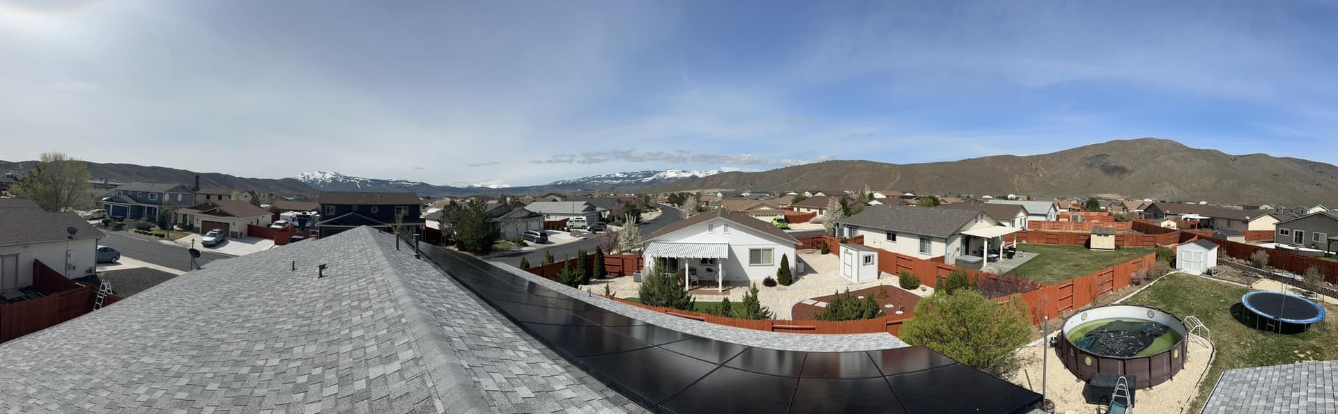 A panoramic view of a residential area with a roof in the foreground and mountains in the background.