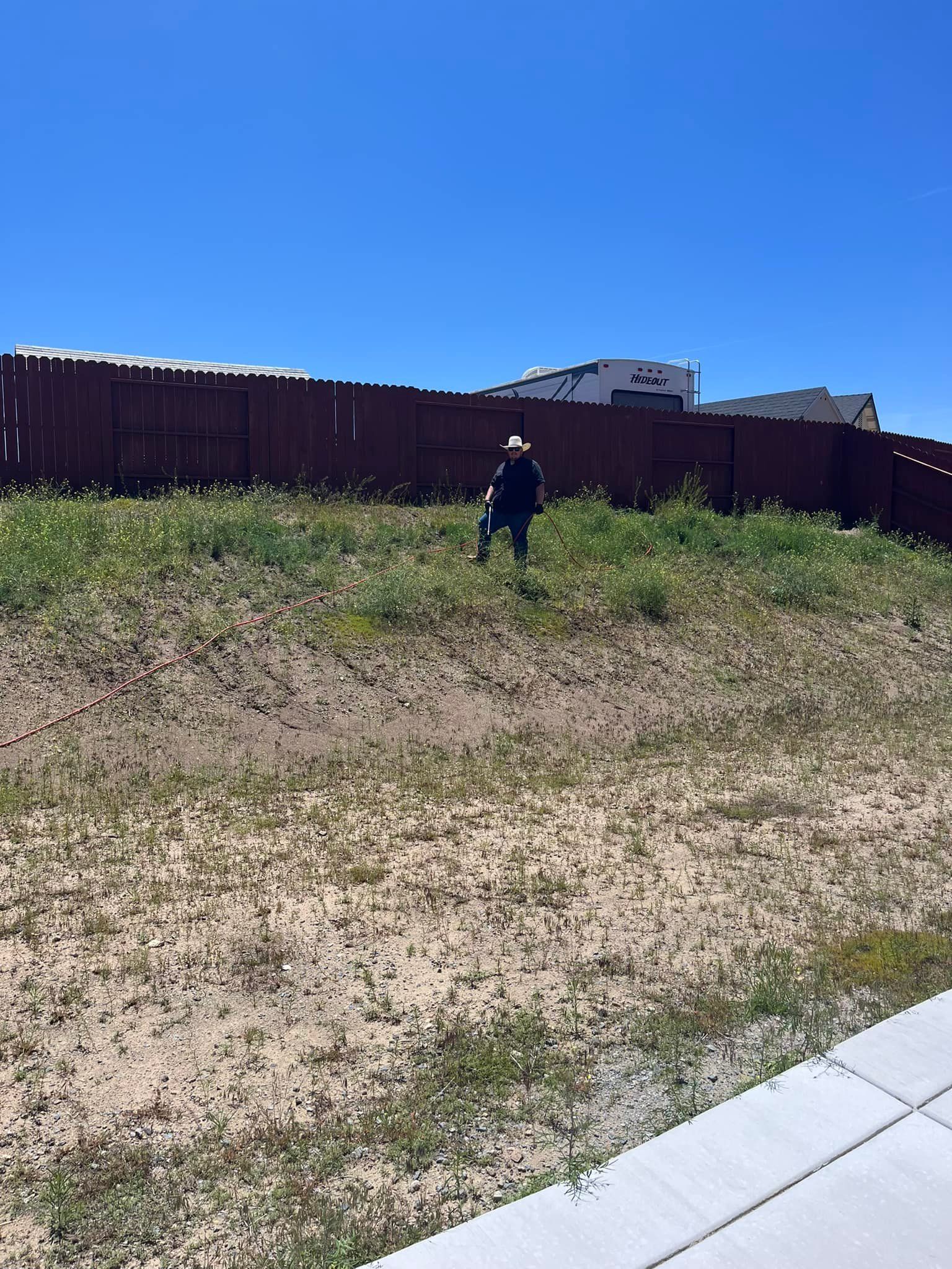A man is standing in a grassy field next to a fence.