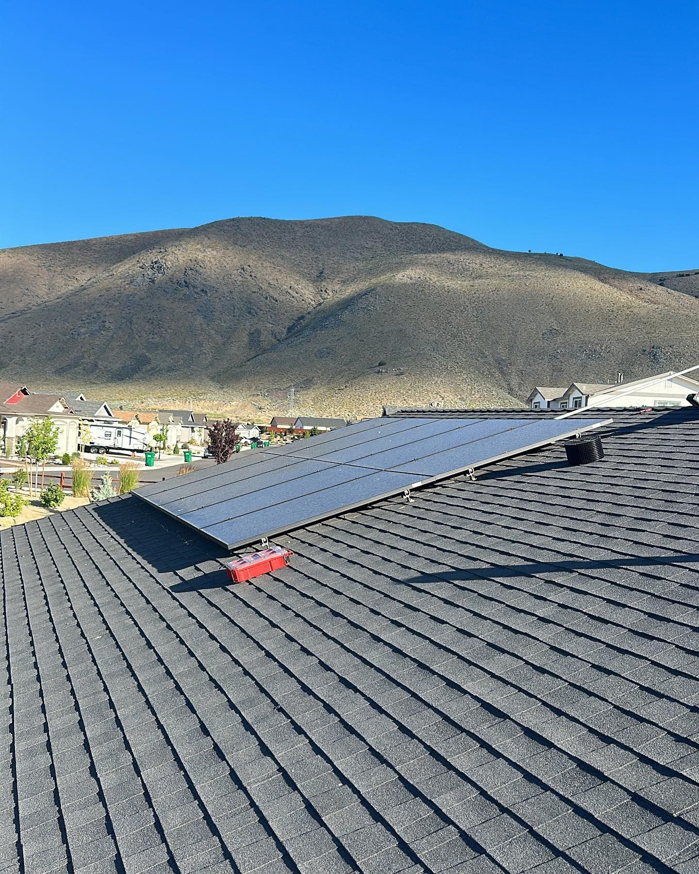 A solar panel is sitting on top of a roof with mountains in the background.