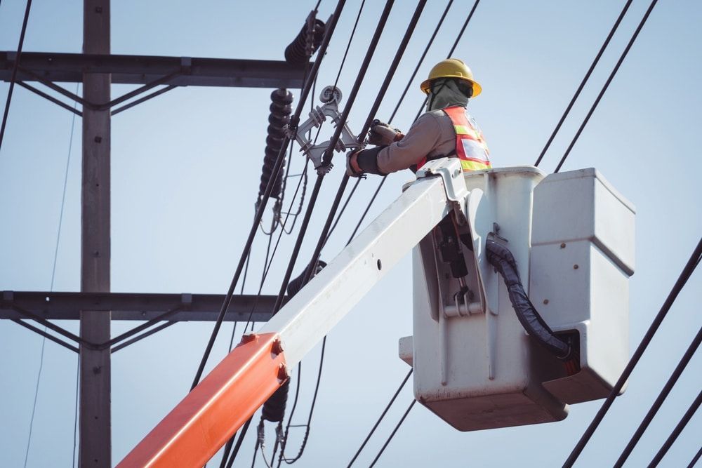 A Man Is Working On A Power Line In A Bucket — AA Electrical Co in Yeppoon, QLD