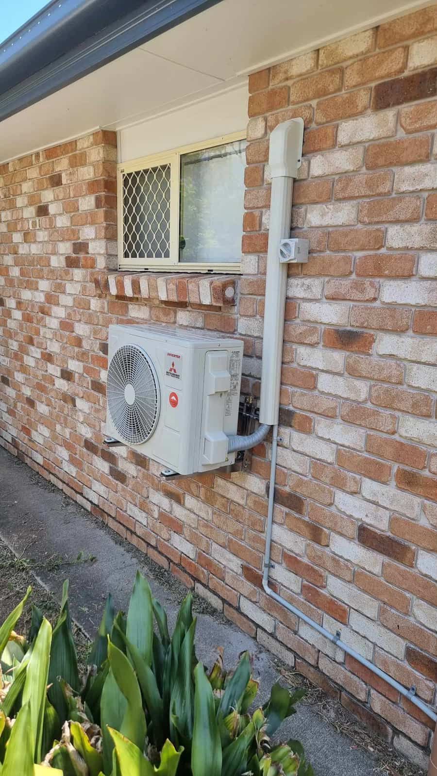 An Air Conditioner Is Installed On The Side Of A Brick Building — AA Electrical Co in Yeppoon, QLD