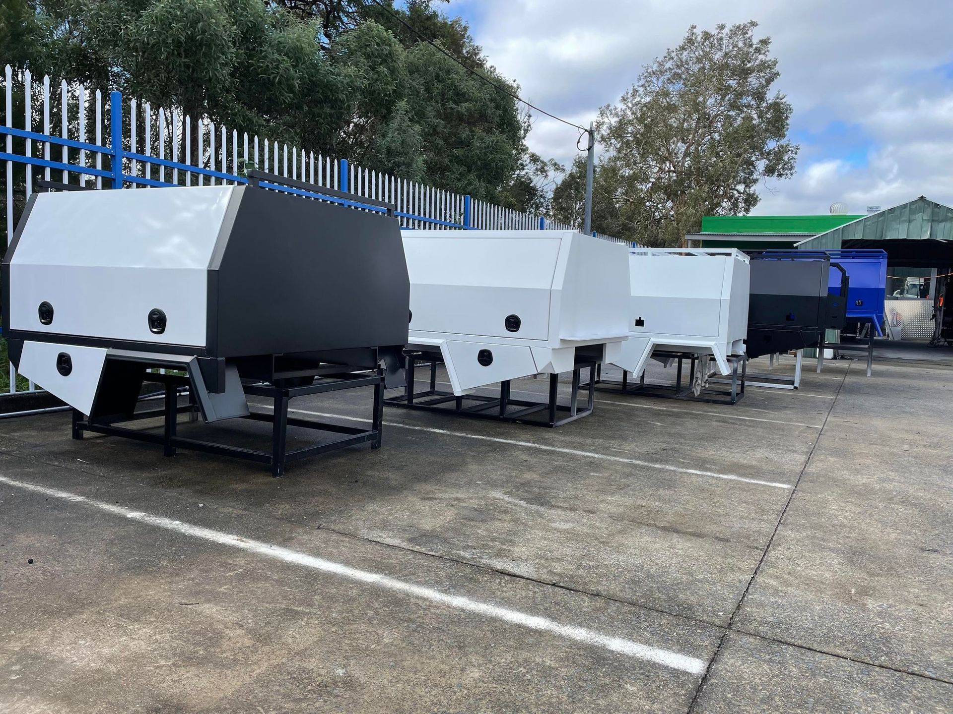 Several Truck Bed Canopies in Black and White Are on Display Outside On a Paved Area — PT Canopy In Slacks Creek, QLD