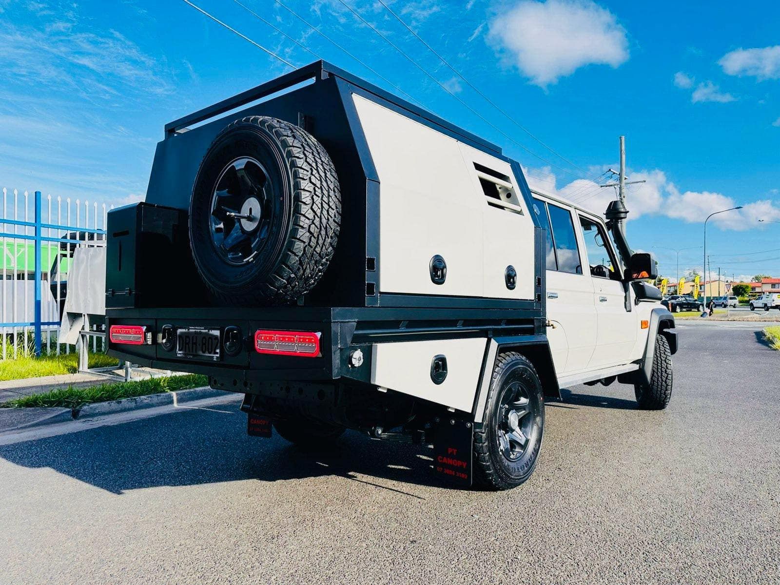 White Pickup Truck With a Black Camper Shell and Spare Tire, Parked on Pavement — PT Canopy In Slacks Creek, QLD