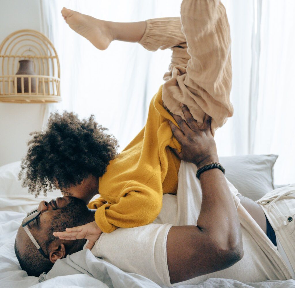 A man is laying on a bed holding a child on his back.
