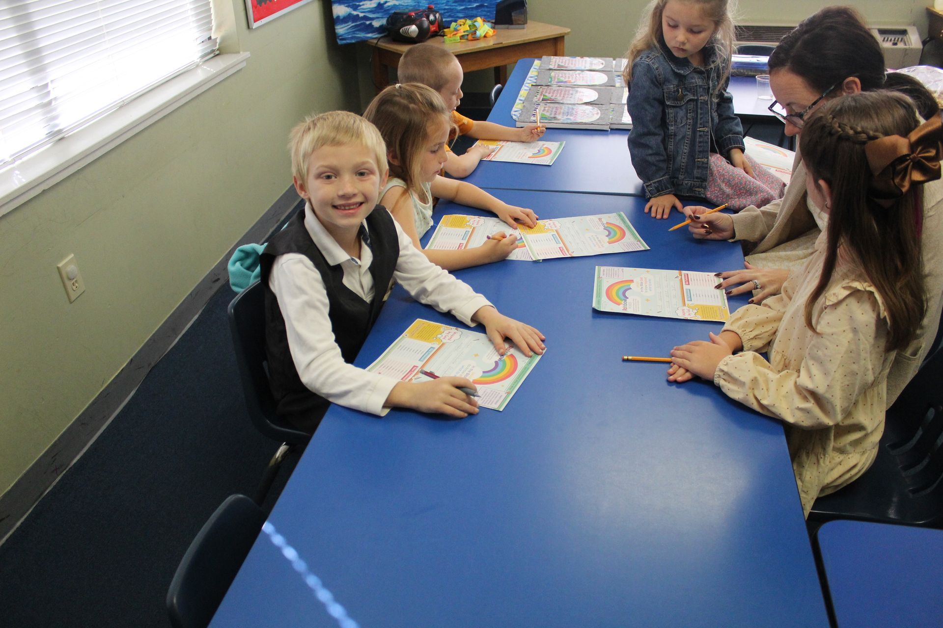 A group of children are sitting at blue tables in a classroom.