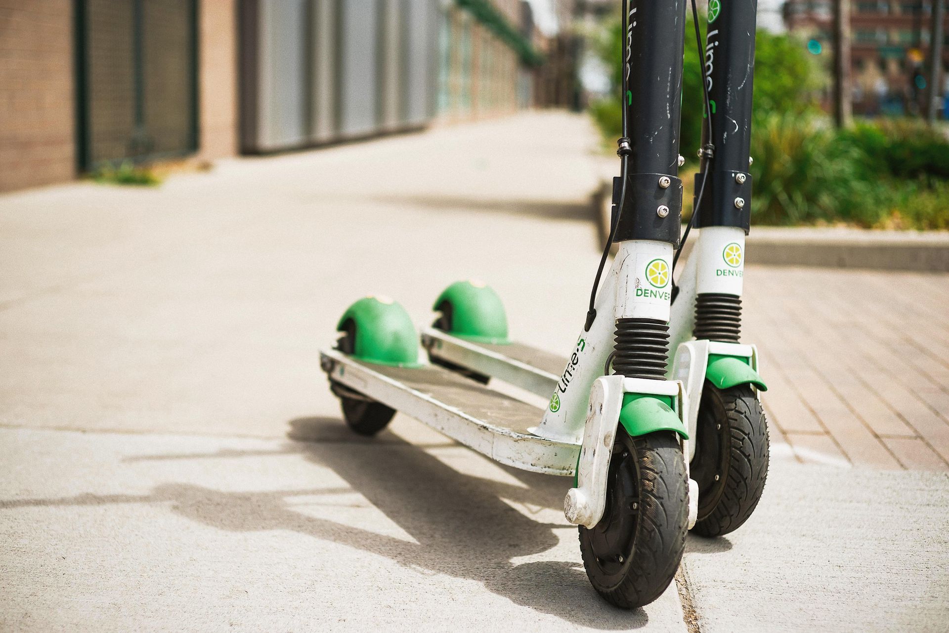 Two green and white Lime scooters parked on a sidewalk, casting shadows.