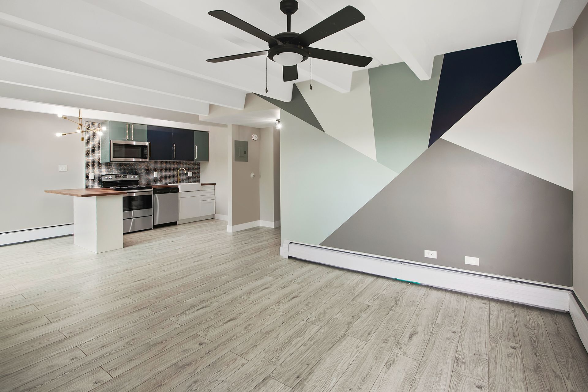 Modern apartment interior with kitchen, geometric accent wall, and ceiling fan.