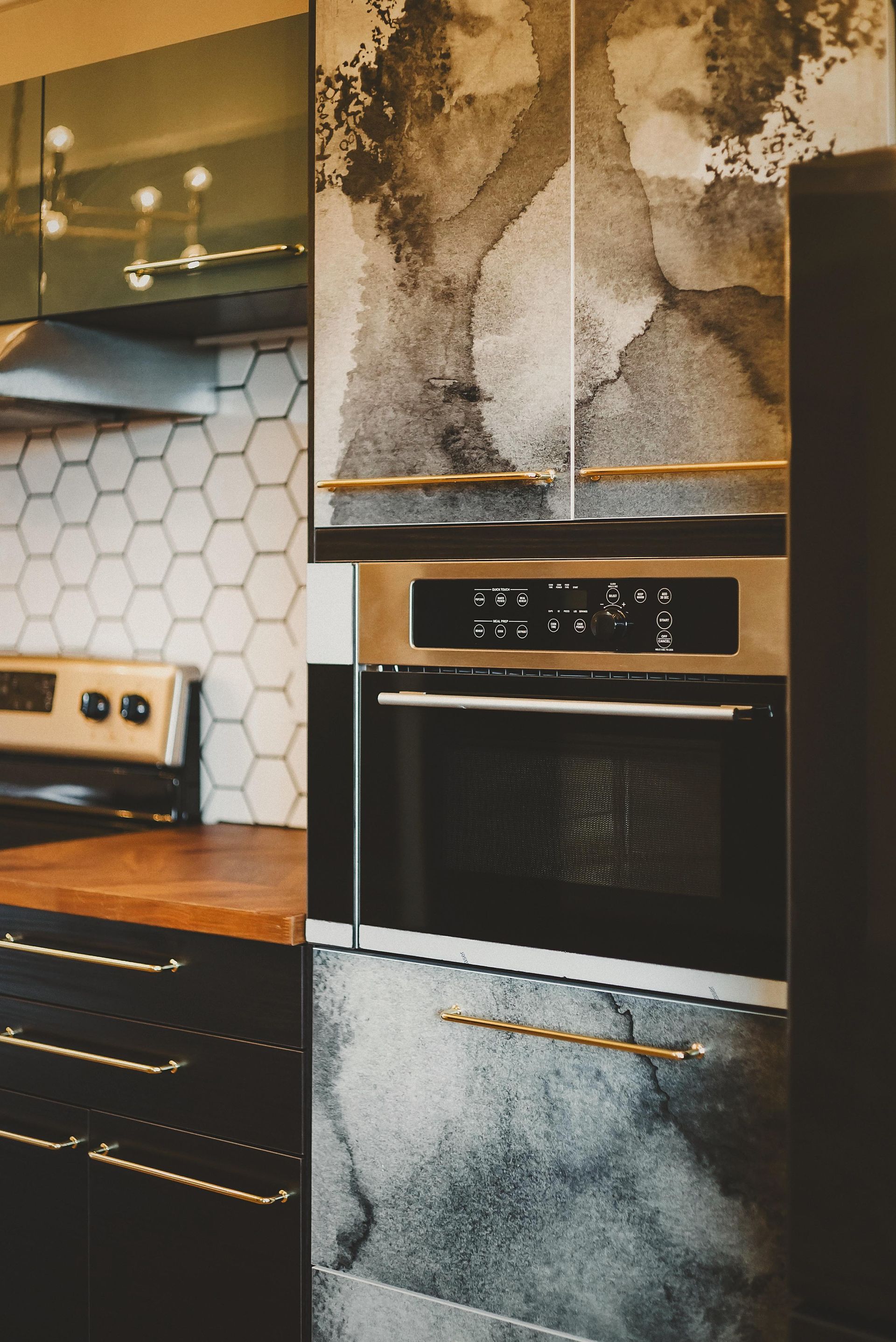 Kitchen with abstract watercolor-patterned cabinets, gold hardware, and stainless steel oven and stovetop.