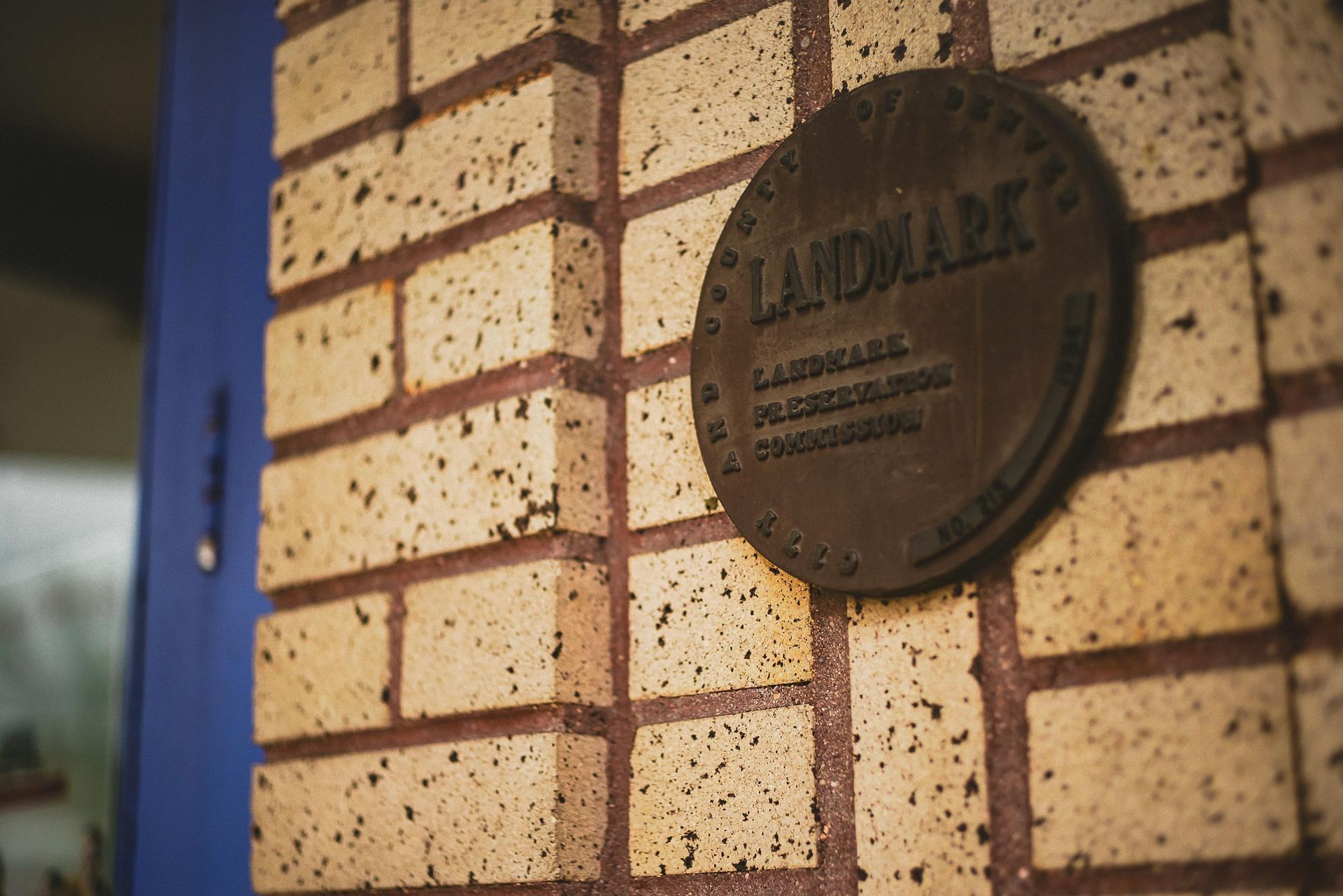 Brown landmark plaque on a brick wall next to a blue door.