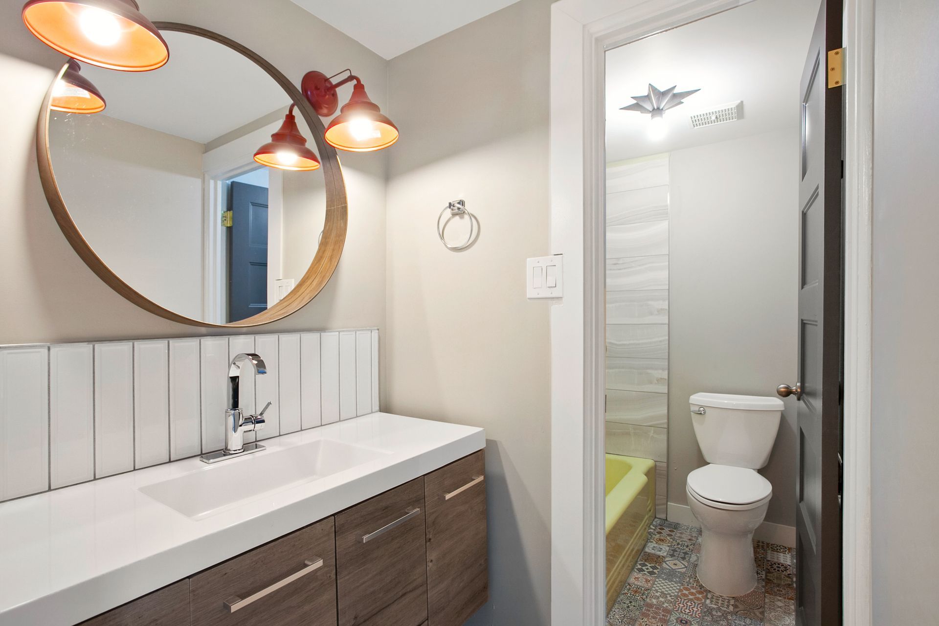 Bathroom with a vanity, round mirror, and open doorway to a toilet and shower.