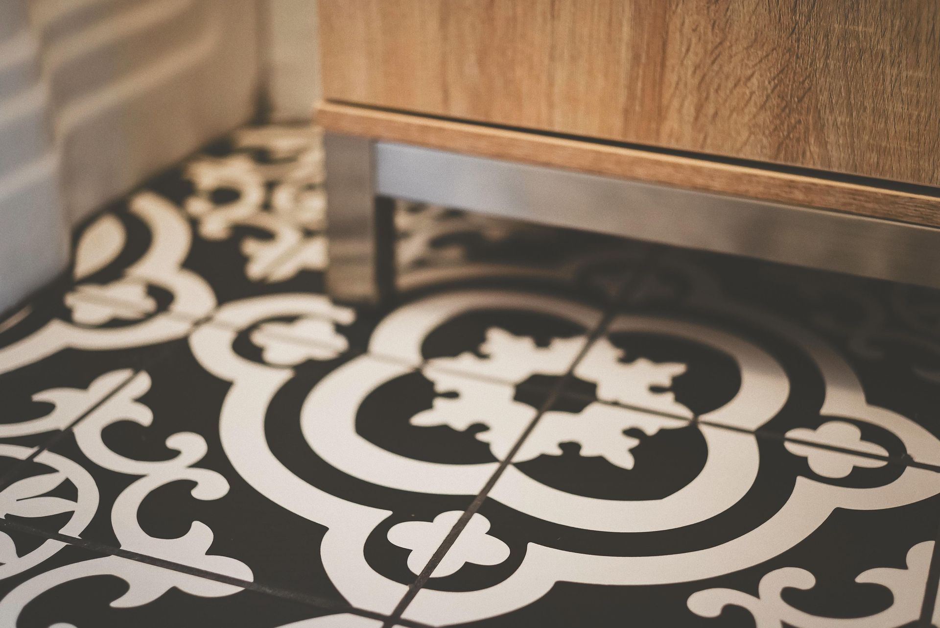 Black and white patterned floor tiles beneath a wooden cabinet with stainless steel legs.