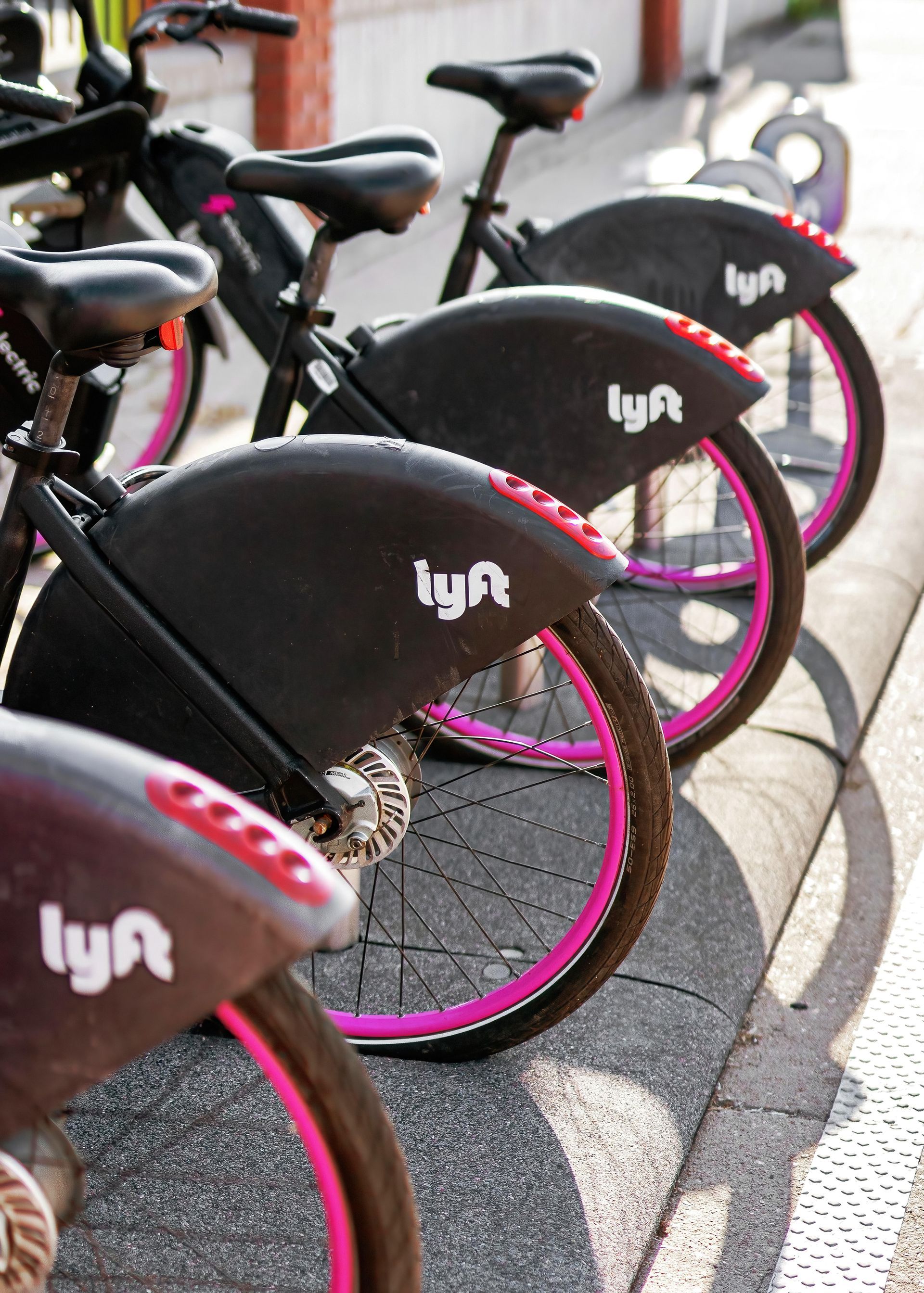 Lyft bike share bikes parked along a curb; black bikes with pink wheels.