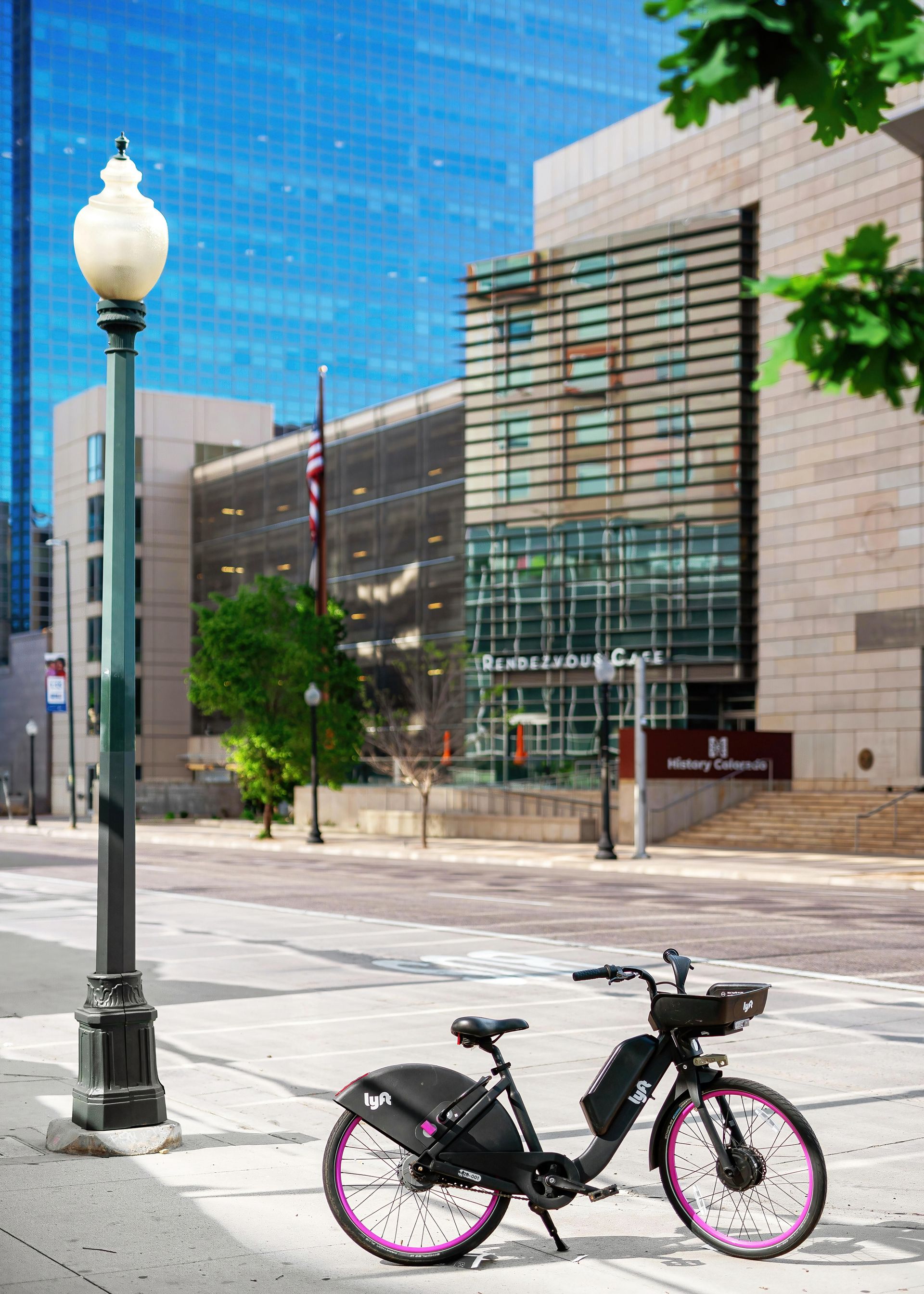 Black bicycle with pink rims on a city sidewalk, with a building in the background.