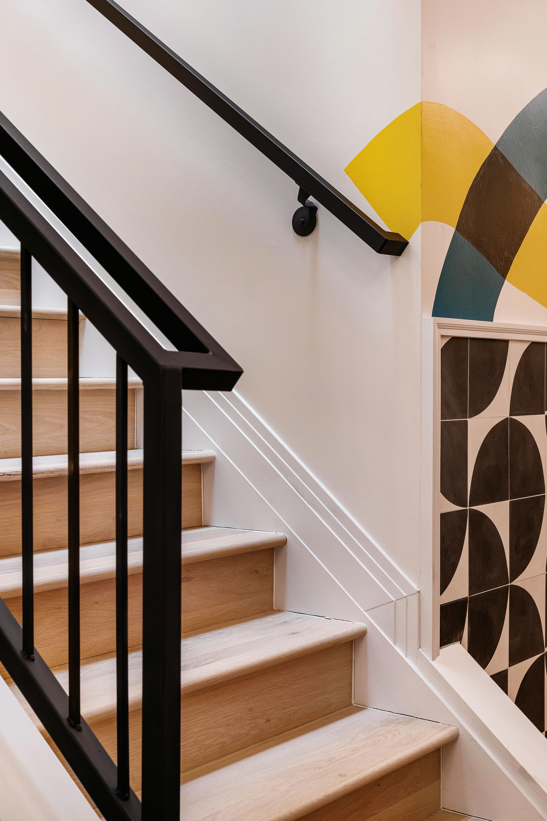 Staircase with black railing, white walls, and a patterned mural.