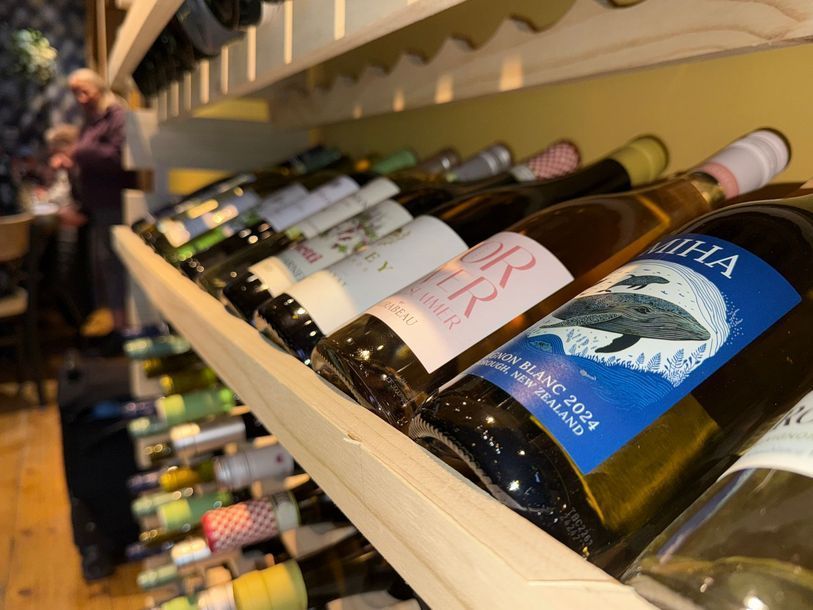 Wine bottles on a wooden shelf with a person blurred in the background