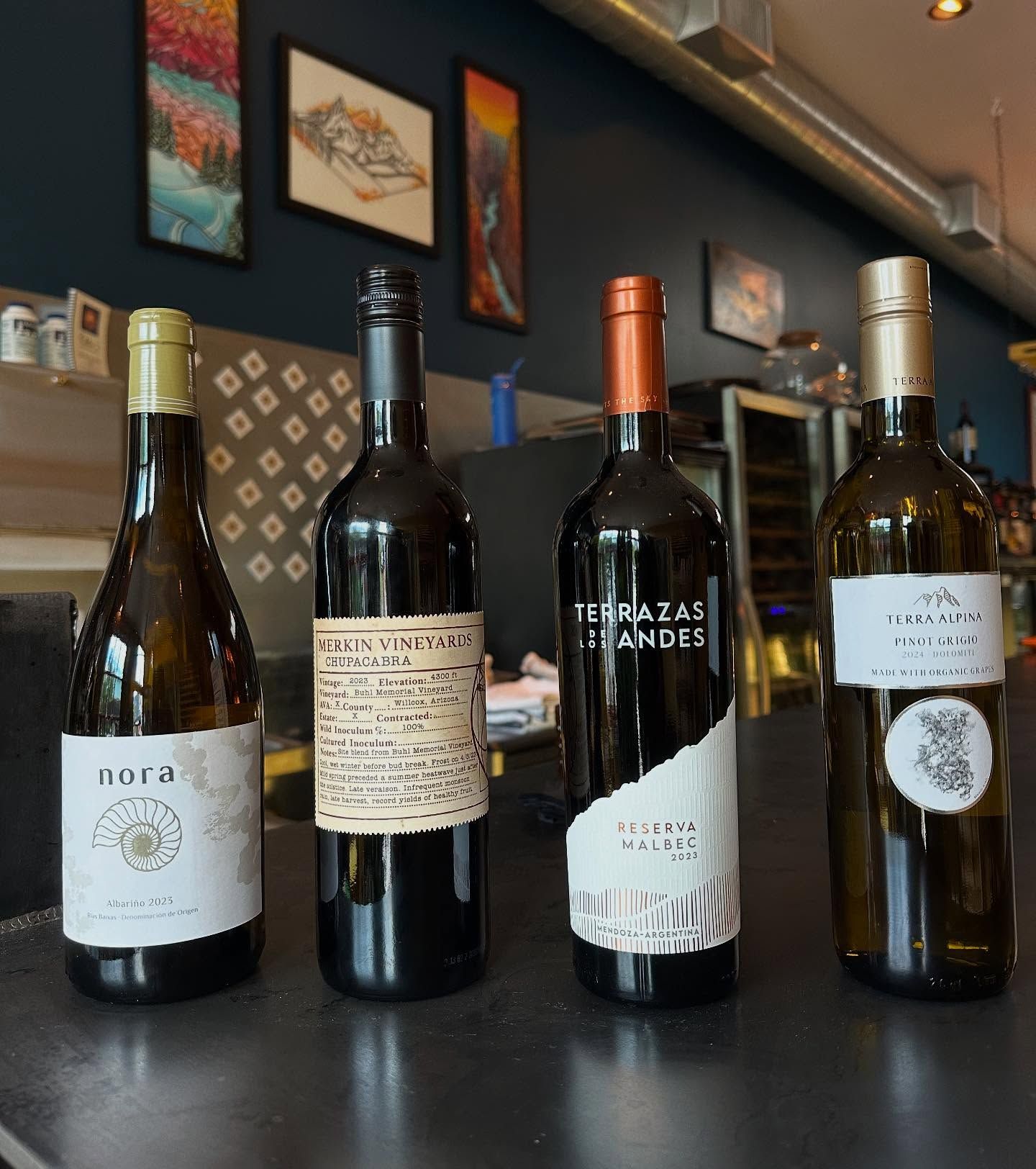 Four wine bottles with various labels stand on a bar