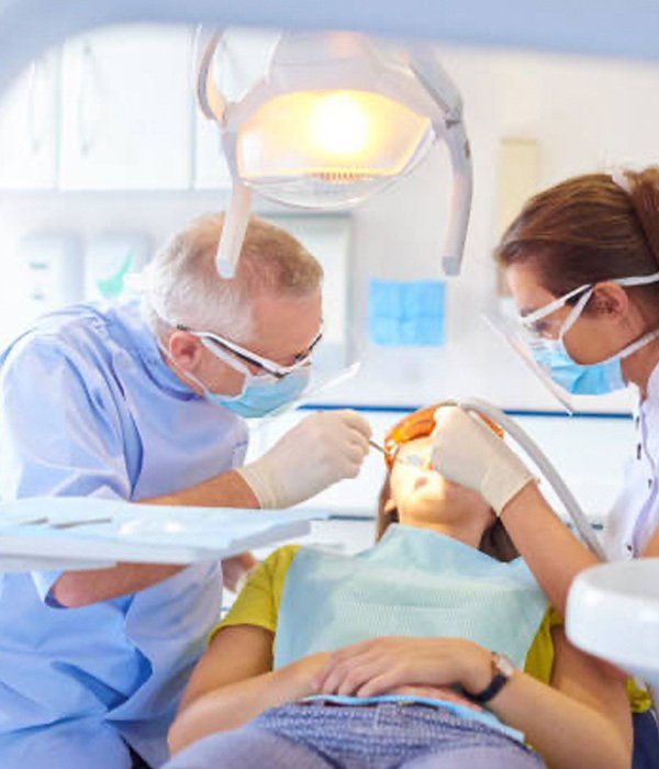 A woman is getting her teeth examined by two dentists