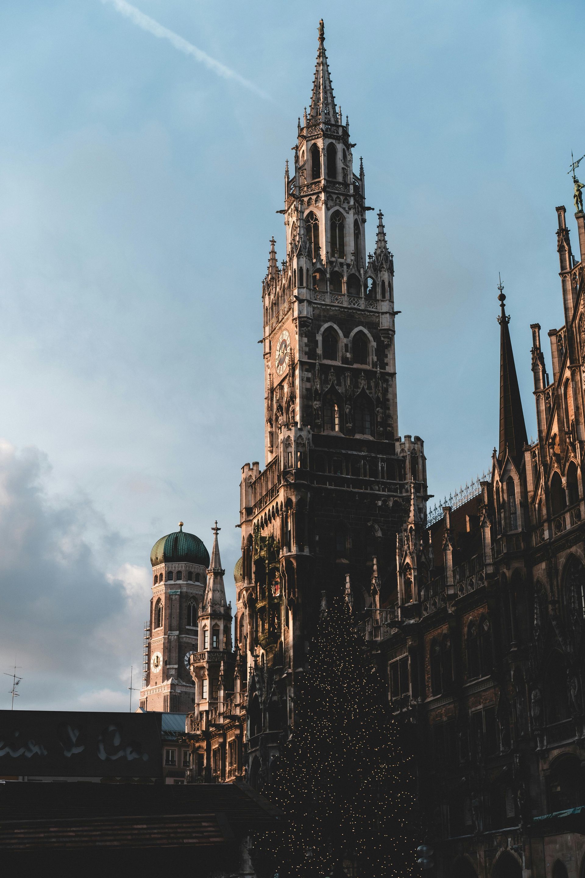 Tall, ornate clock tower of Neues Rathaus (New Town Hall) in Munich, Germany, with a Christmas tree in the foreground.