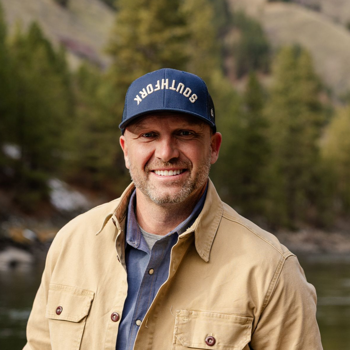 A bald man wearing glasses and a blue jacket is smiling for the camera.