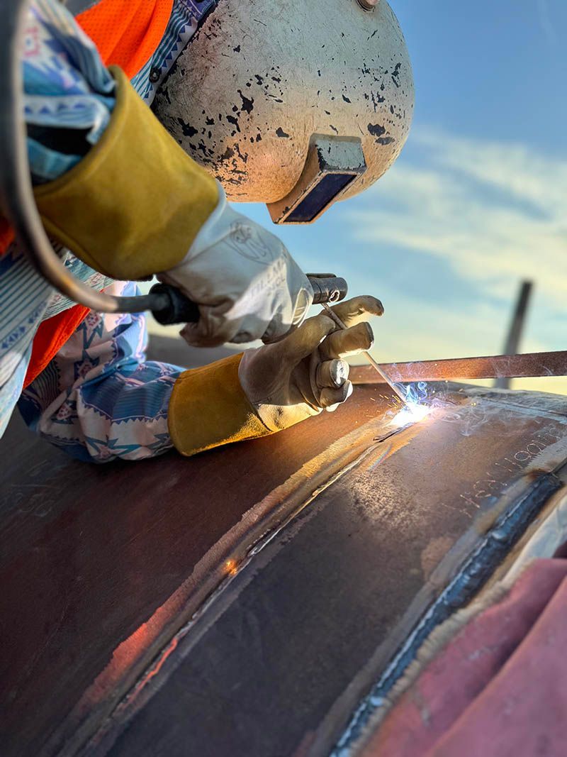 A man wearing a helmet and gloves is welding a piece of metal.