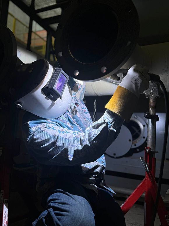 A man wearing a welding mask is welding a pipe.