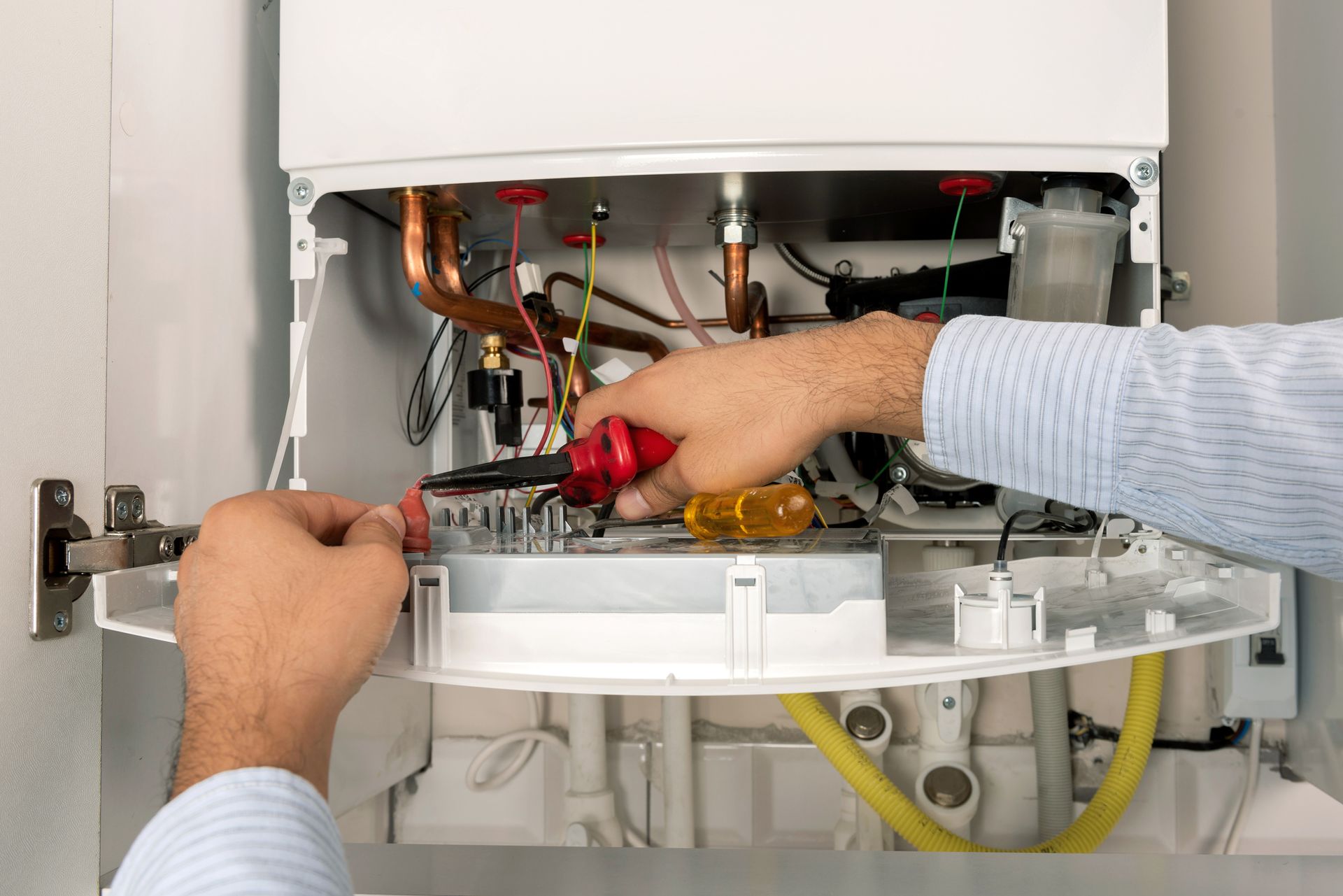 Hands of a technician working on the internal components of a gas boiler with tools.