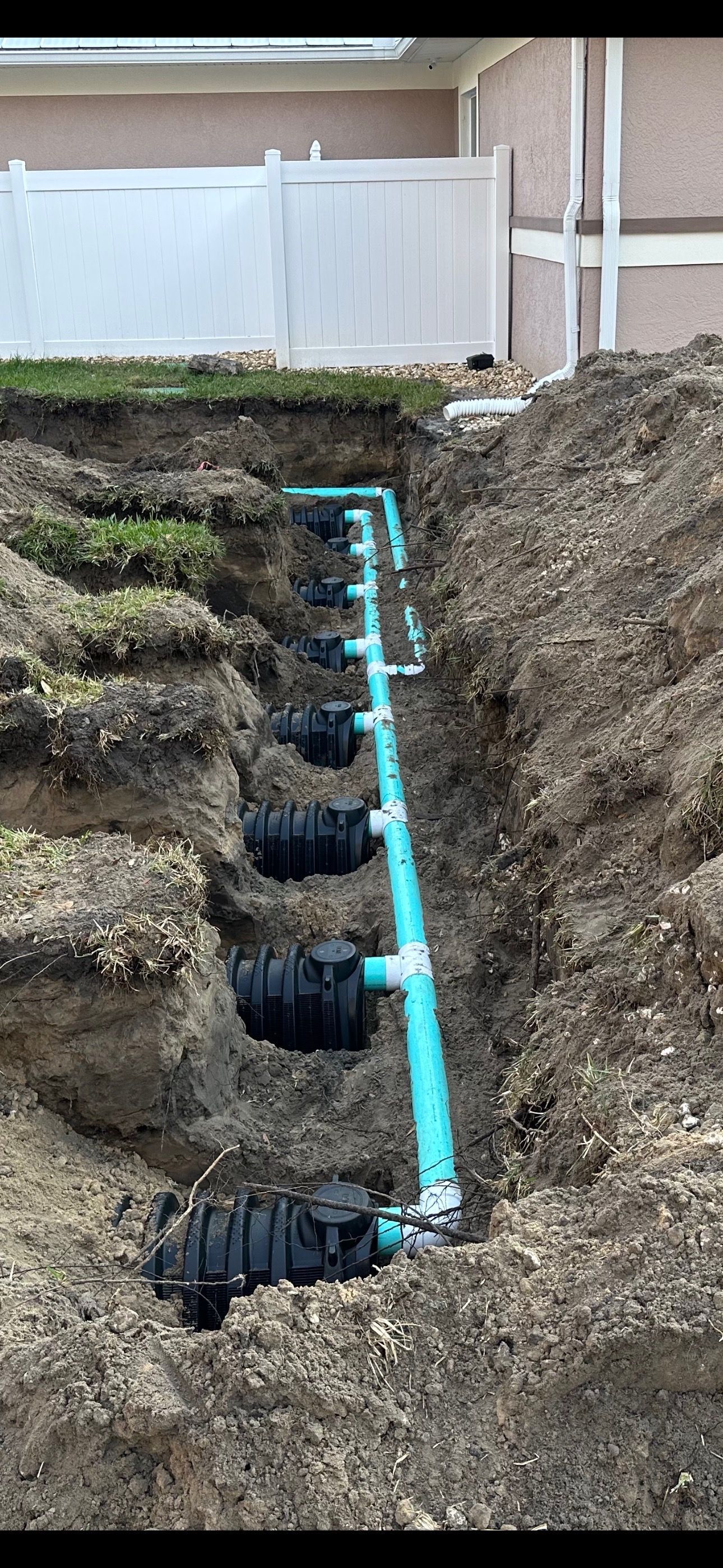 A septic system is being installed in the dirt next to a house.
