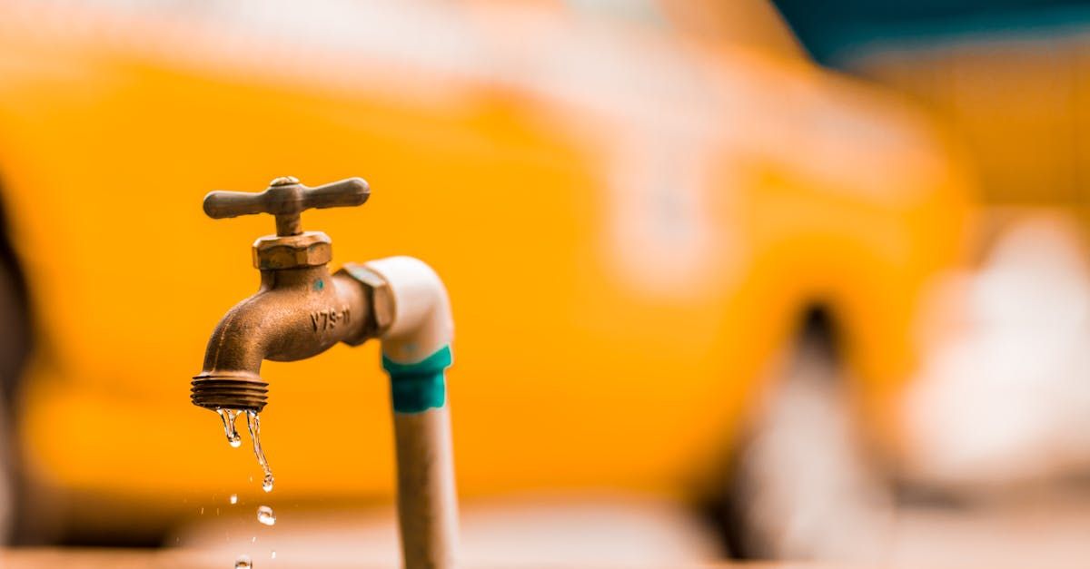 A close up of a faucet with water dripping from it in front of a yellow car.
