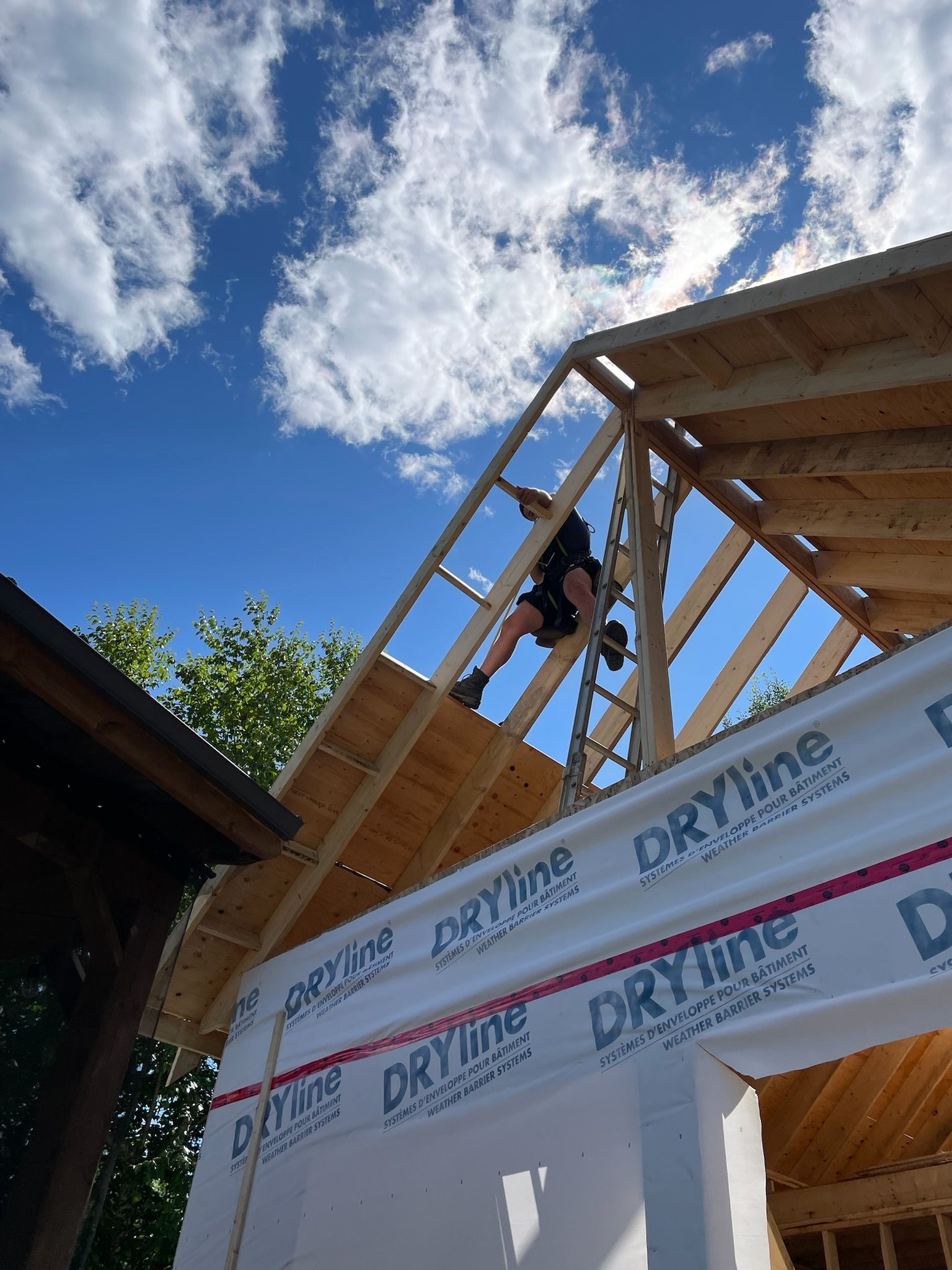 Ouvrier du bâtiment sur la charpente du toit, installant le revêtement. Ciel bleu avec des nuages, journée ensoleillée.