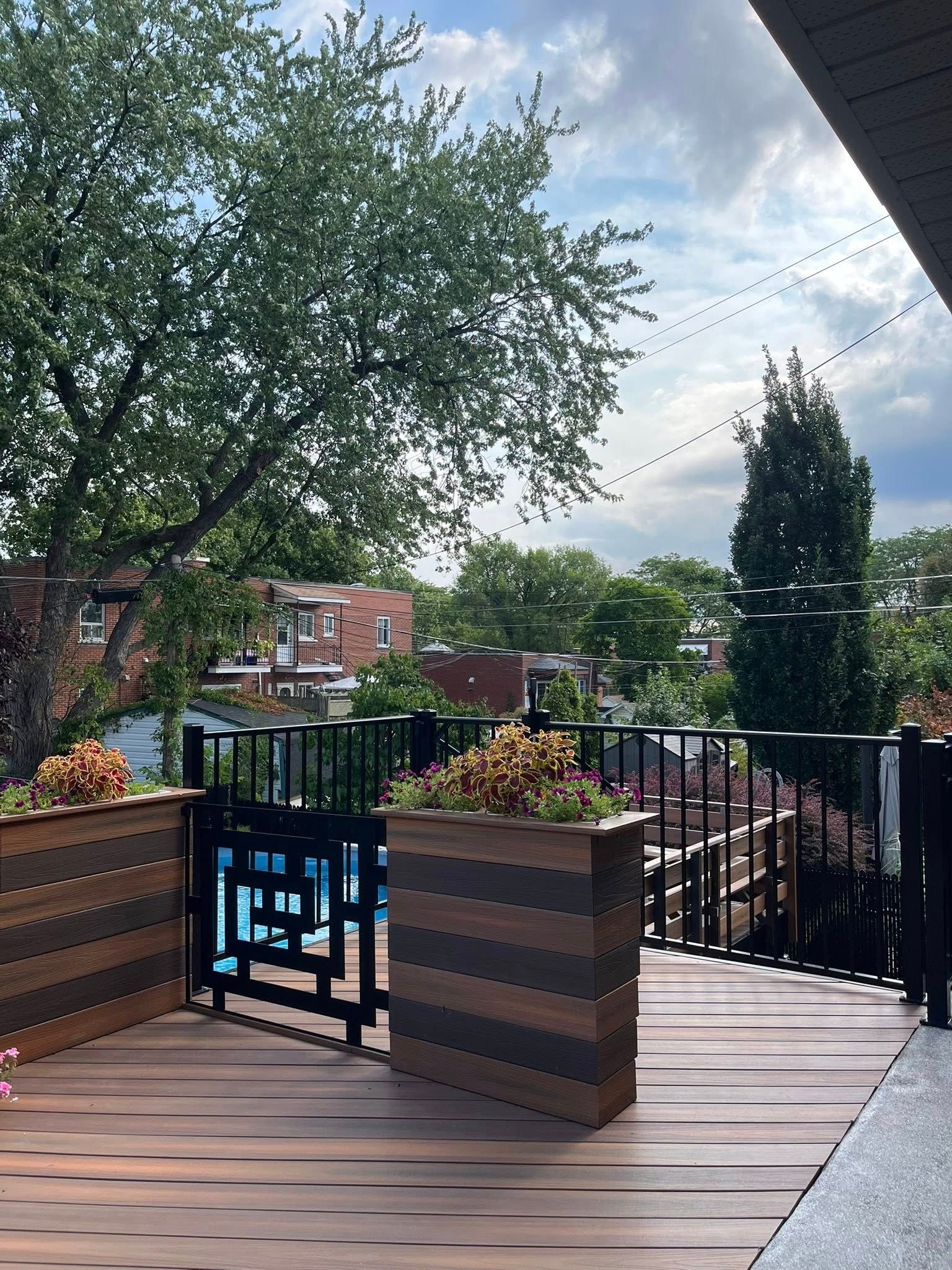 Terrasse en bois avec rambarde en métal foncé, donnant sur un quartier. Jardinière avec des plantes.