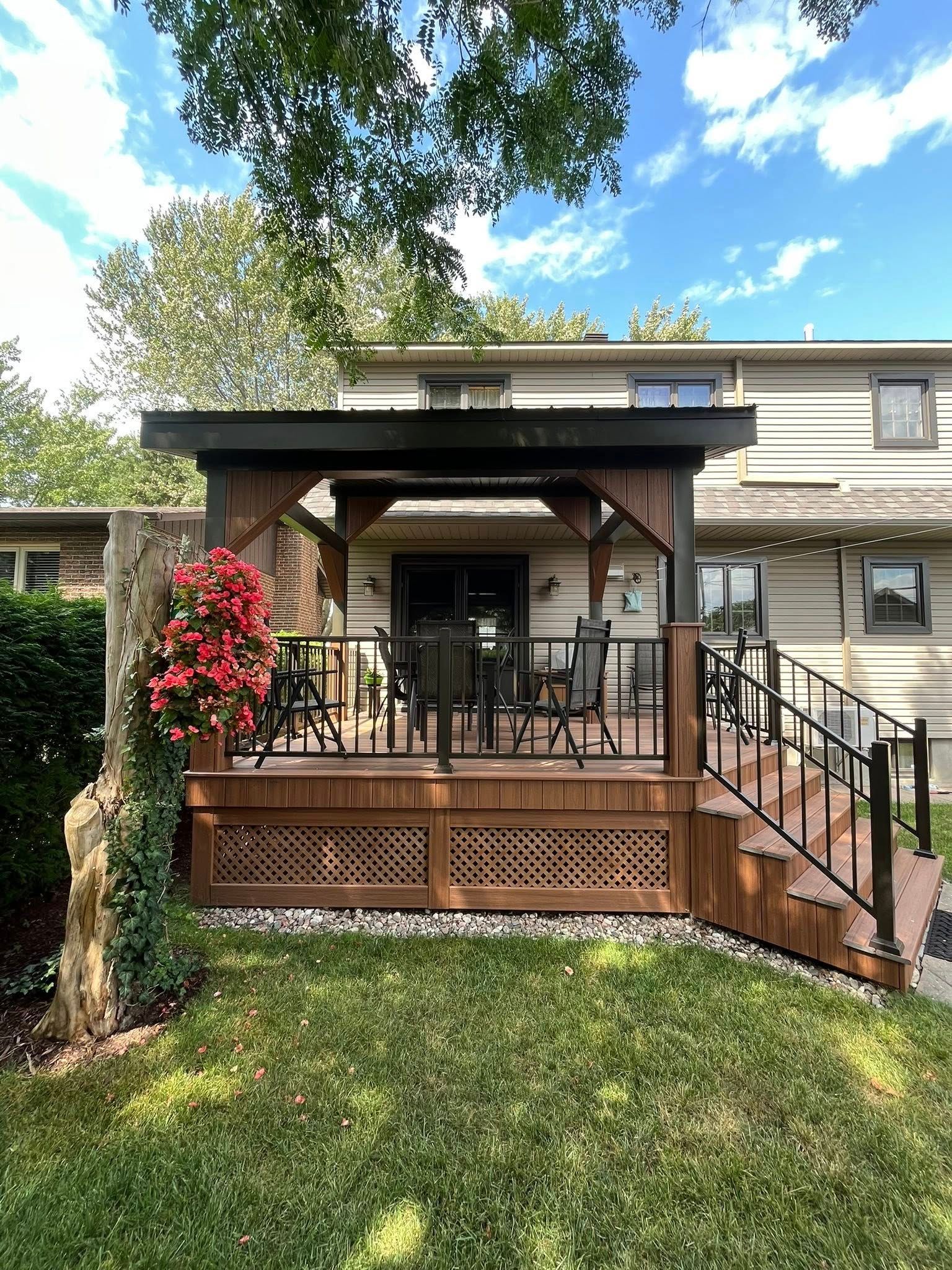 Terrasse en bois avec pergola, rambarde noire, détails en treillis et mobilier de jardin dans un jardin.