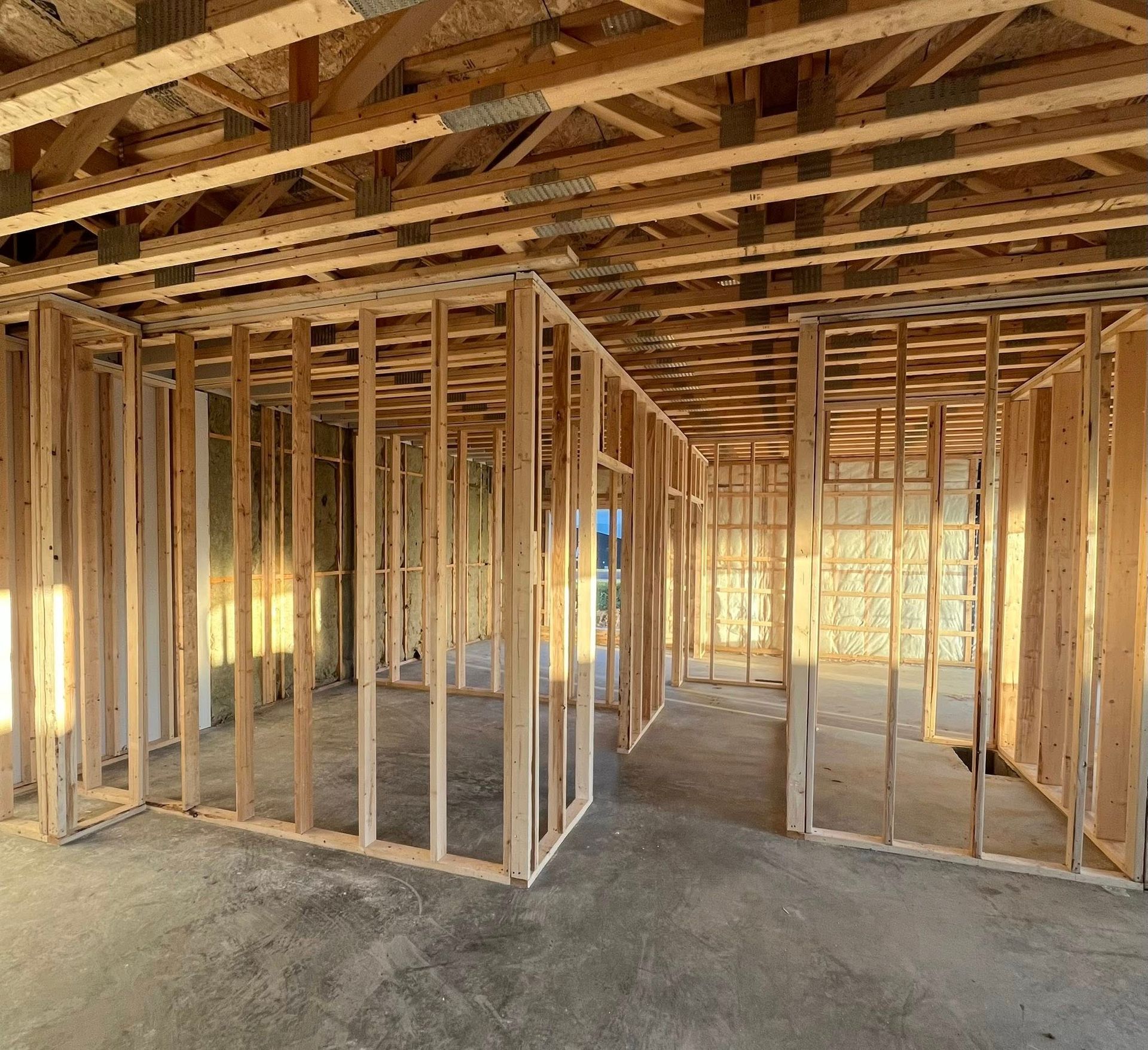 Charpente intérieure en bois d'un bâtiment en construction, montrant les murs, les poutres du plafond et le sol en béton.