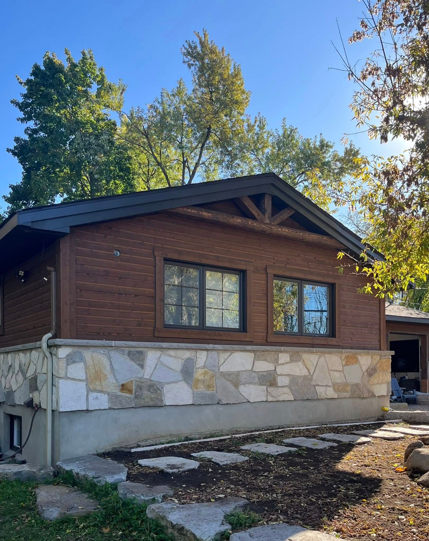 Bâtiment en briques avec soubassement en pierre, boiseries sombres, fenêtres et arbres par une journée ensoleillée.