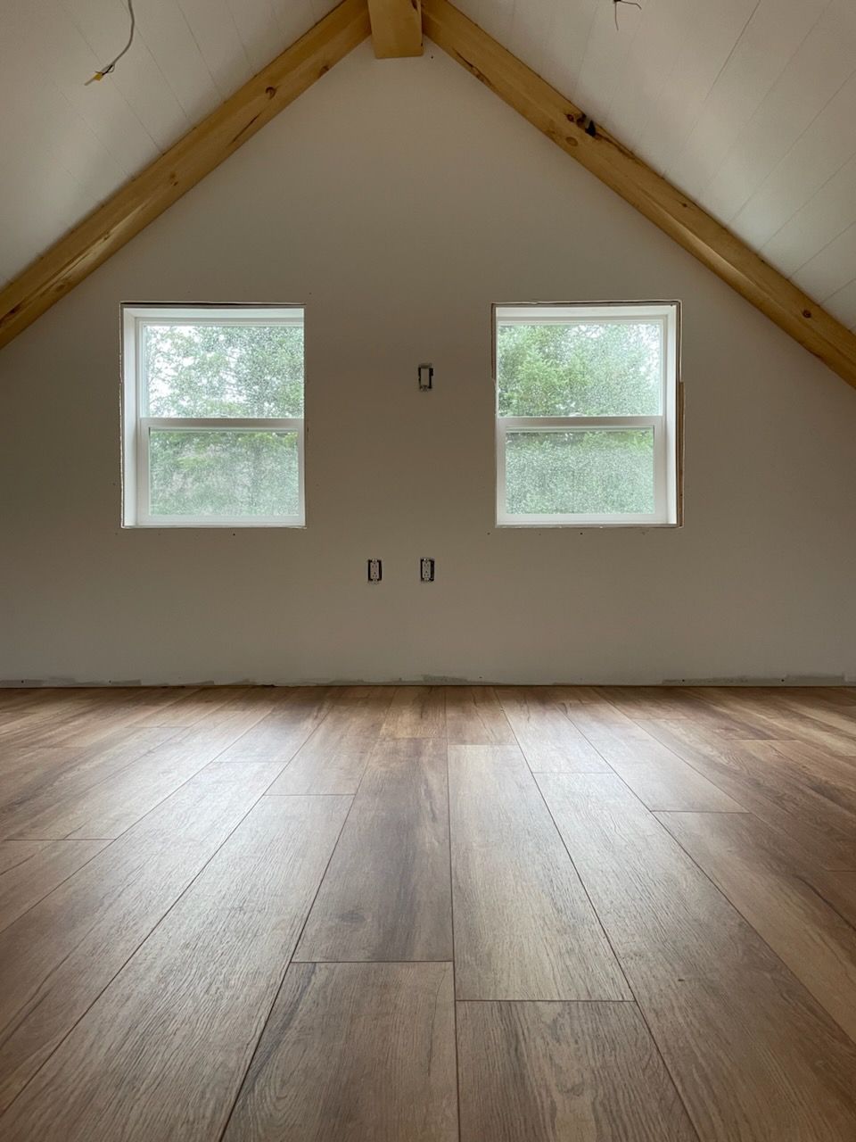 Intérieur du grenier avec plancher en bois, deux fenêtres et poutres apparentes.